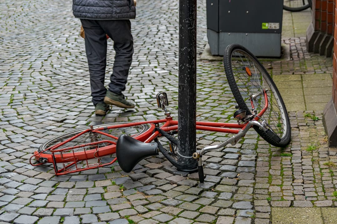 Red bicycle fallen on wet cobblestone street, person walking past.