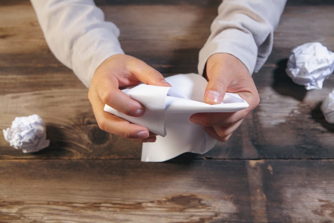 Hands crumpling paper on a wooden desk.
